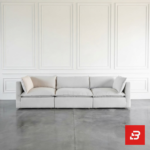 Front interior view of a luxury upholstered minimalist sectional sofa in off white velvet fabric featuring plush cushions and contrasting throw pillows against a white wall paneling background by Bahoo Furniture UAE