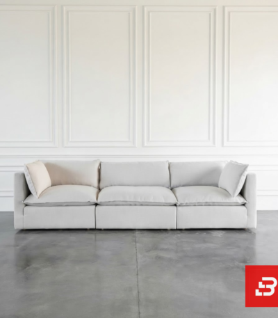 Front interior view of a luxury upholstered minimalist sectional sofa in off white velvet fabric featuring plush cushions and contrasting throw pillows against a white wall paneling background by Bahoo Furniture UAE