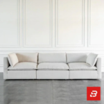 Front interior view of a luxury upholstered minimalist sectional sofa in off white velvet fabric featuring plush cushions and contrasting throw pillows against a white wall paneling background by Bahoo Furniture UAE