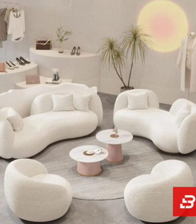Stylized boutique showroom view of a luxury upholstered organic curved lounge set in off white bouclé fabric featuring matching curved sofas, armchairs, and nested round coffee tables by Bahoo Furniture UAE