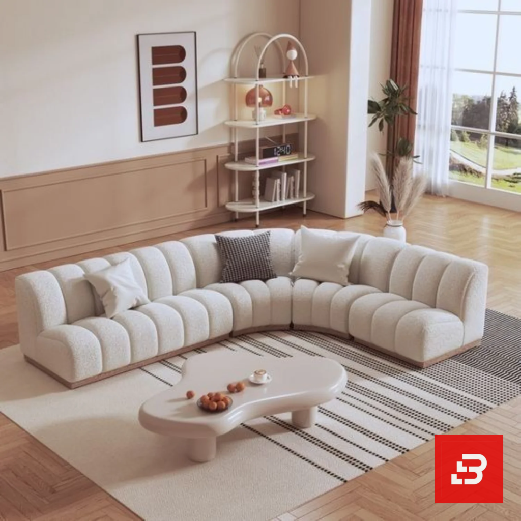 Sunlit interior view of a luxury upholstered curved channel sectional sofa in off white bouclé fabric featuring rhythmic fluted tufting and an organic coffee table by Bahoo Furniture UAE