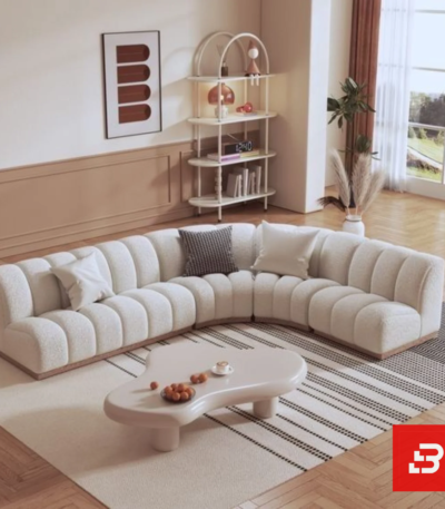 Sunlit interior view of a luxury upholstered curved channel sectional sofa in off white bouclé fabric featuring rhythmic fluted tufting and an organic coffee table by Bahoo Furniture UAE