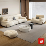 Bright modern living room view of a luxury upholstered contemporary sofa set in off white velvet fabric featuring a 3-seater sofa, matching armchair, pouf, and round nesting coffee tables by Bahoo Furniture UAE
