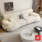 Bright modern living room view of a luxury upholstered contemporary sofa set in off white velvet fabric featuring a 3-seater sofa, matching armchair, pouf, and round nesting coffee tables by Bahoo Furniture UAE