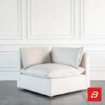 Studio interior view of a luxury upholstered modular corner lounge chair in off white velvet fabric featuring a plush back cushion and side armrest against a white wall paneling background by Bahoo Furniture UAE