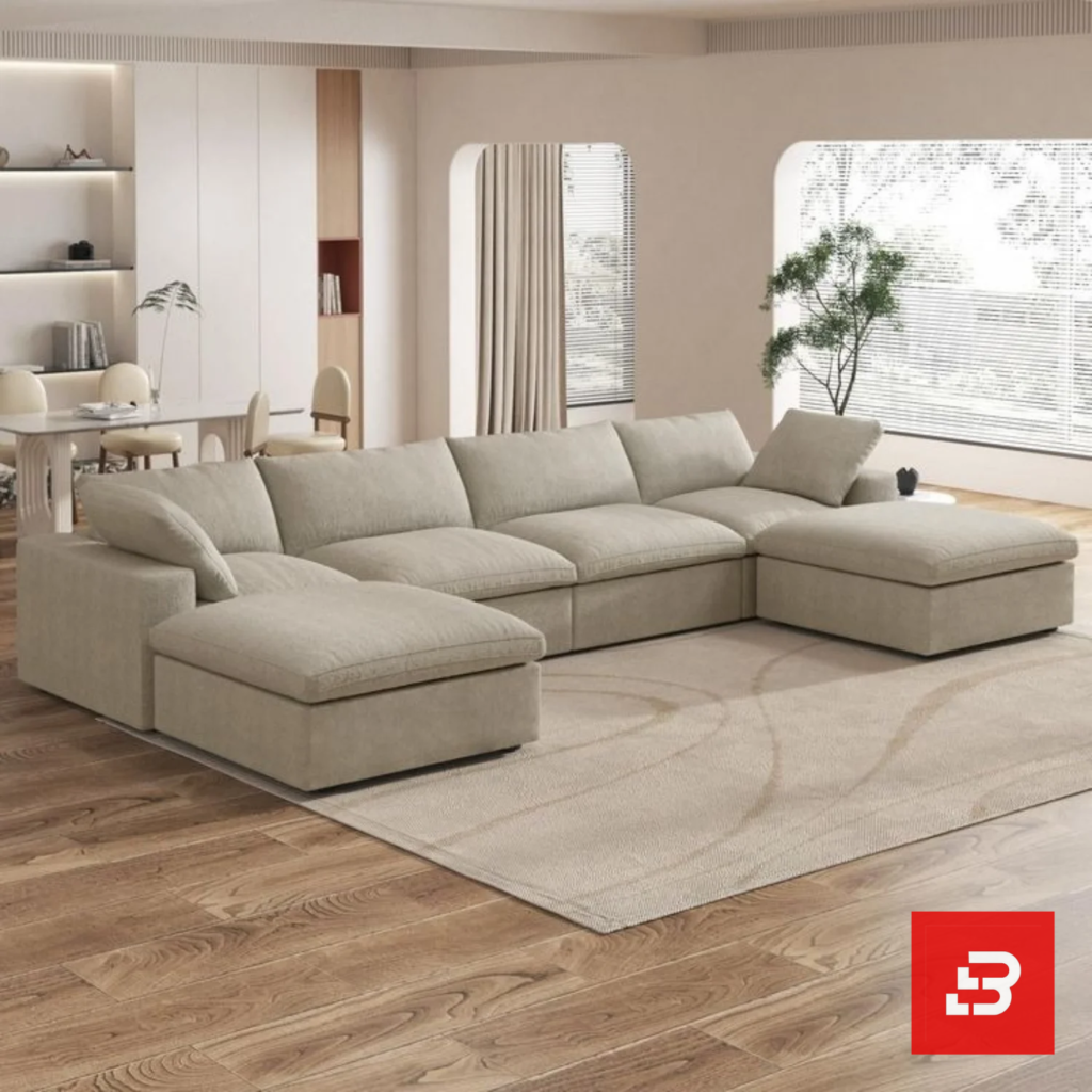 Sunlit interior view of a luxury upholstered modular u-shape sectional sofa in beige velvet fabric featuring dual ottomans and plush modular cushioning in an open-plan living room by Bahoo Furniture UAE