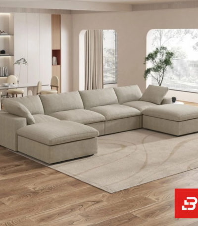Sunlit interior view of a luxury upholstered modular u-shape sectional sofa in beige velvet fabric featuring dual ottomans and plush modular cushioning in an open-plan living room by Bahoo Furniture UAE