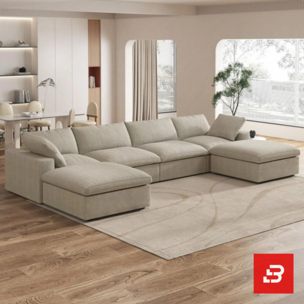 Sunlit interior view of a luxury upholstered modular u-shape sectional sofa in beige velvet fabric featuring dual ottomans and plush modular cushioning in an open-plan living room by Bahoo Furniture UAE