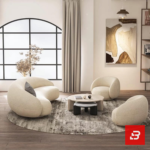 Stunning seaside modern luxury living room interior view of a luxury curved asymmetric sofa upholstered in textured off white bouclé fabric featuring a matching armchair and golden round coffee table by Bahoo Furniture UAE