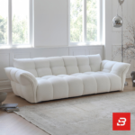 Sunlit minimal modern apartment living room interior view of a luxury channel tufted sofa upholstered in textured off white bouclé fabric featuring structured vertical channel tufting and flared cushioned armrests by Bahoo Furniture UAE