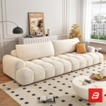 Bright modern sunlit apartment living room interior view of a luxury grid-tufted modular lounge set upholstered in textured off white bouclé fabric featuring block-stitched modular sofa, matching armchair, and footstool ottoman by Bahoo Furniture UAE