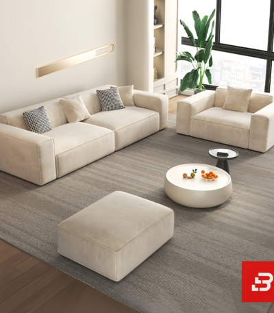 Sunlit minimal modern urban apartment living room interior view of a luxury block modular sectional upholstered in plush velvet fabric featuring a modular 3-seater sofa, matching armchair, ottoman, and round coffee table by Bahoo Furniture UAE