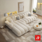 Sunlit minimal modern apartment living room interior view of a luxury channel tufted sectional upholstered in textured off white bouclé fabric featuring a generous chaise lounge and matching barrel armchair by Bahoo Furniture UAE