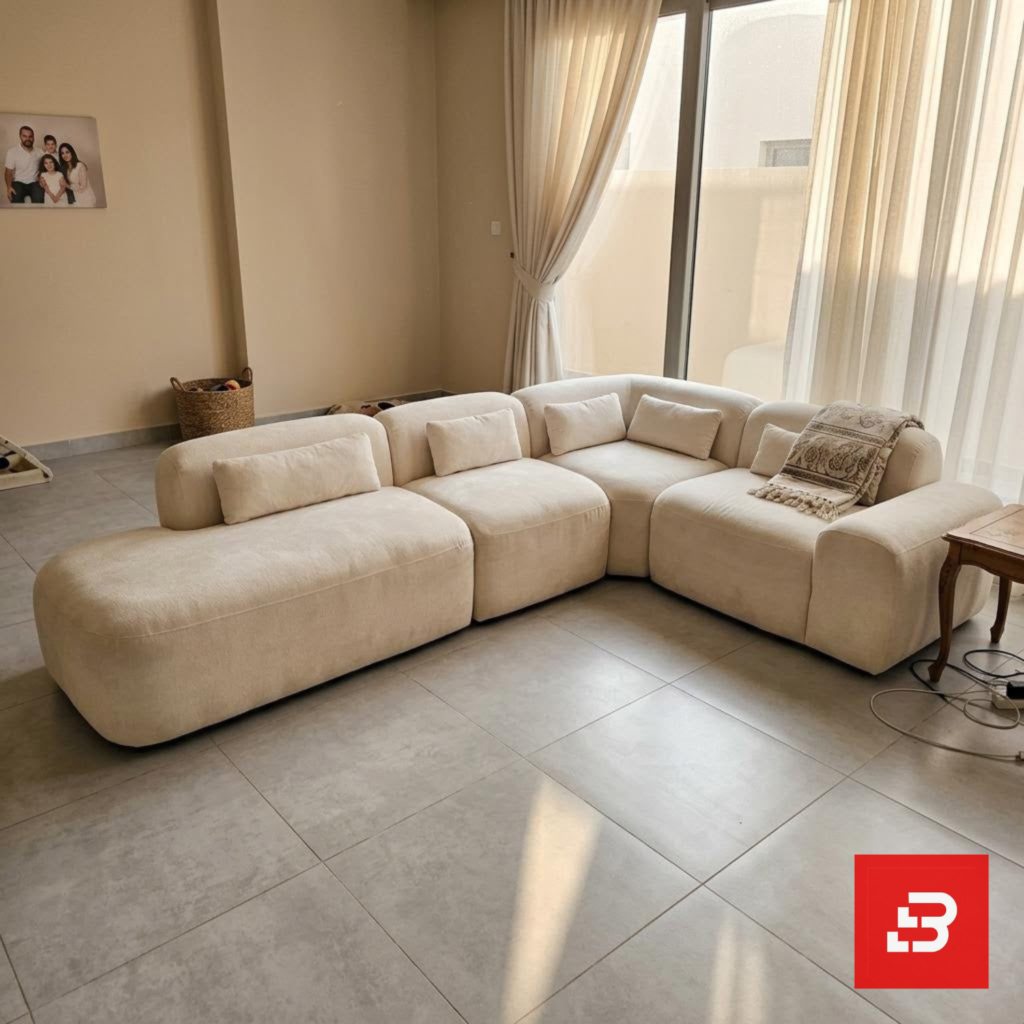 Bright natural light modern luxury living room interior view of a luxury modular sectional upholstered in textured beige bouclé fabric featuring low-profile modular corner seating, bolster pillows, and a patterned throw blanket by Bahoo Furniture UAE