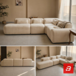 Bright natural light modern luxury living room interior view of a luxury modular sectional upholstered in textured beige bouclé fabric featuring low-profile modular corner seating, bolster pillows, and a patterned throw blanket by Bahoo Furniture UAE