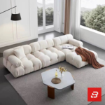 Sunlit minimal modern apartment living room interior view of a luxury segmented cushion sectional upholstered in textured off white bouclé fabric featuring pillowed modular segments and an extended chaise lounge by Bahoo Furniture UAE