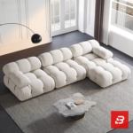 Sunlit minimal modern apartment living room interior view of a luxury segmented cushion sectional upholstered in textured off white bouclé fabric featuring pillowed modular segments and an extended chaise lounge by Bahoo Furniture UAE