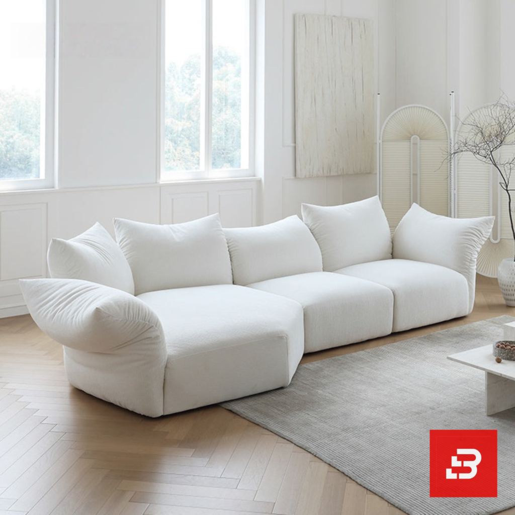 Sunlit minimal modern apartment living room interior view of a luxury cloud sectional upholstered in plush off white bouclé fabric featuring extra-deep lounging cushions and oversized feather-soft scatter pillows by Bahoo Furniture UAE