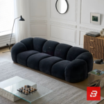 Bright modern minimalist living room interior view of a luxury channel tufted sofa upholstered in textured warm gray bouclé fabric featuring rounded fluted cushions and low-profile armrests by Bahoo Furniture UAE