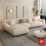 Sunlit minimal modern apartment living room interior view of a luxury fluted sectional upholstered in textured off white bouclé fabric featuring sweeping vertical channel backrests and an extended chaise lounge by Bahoo Furniture UAE