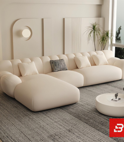 Sunlit minimal modern apartment living room interior view of a luxury fluted sectional upholstered in textured off white bouclé fabric featuring sweeping vertical channel backrests and an extended chaise lounge by Bahoo Furniture UAE