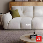 Sunlit warm modern living room interior view of a luxury channel-padded sofa upholstered in textured off white bouclé fabric featuring plush segmented cushioning and stylish contrast scatter cushions by Bahoo Furniture UAE
