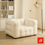 Bright modern cozy living room interior view of a luxury modular armchair upholstered in textured off white bouclé fabric featuring plush channel-tufted square cushioning and low-profile block feet by Bahoo Furniture UAE