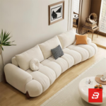 Bright warm modern living room interior showcasing a luxury plissé sectional sofa set upholstered in textured beige bouclé fabric featuring horizontal channel tufting and wooden feet accents by Bahoo Furniture UAE