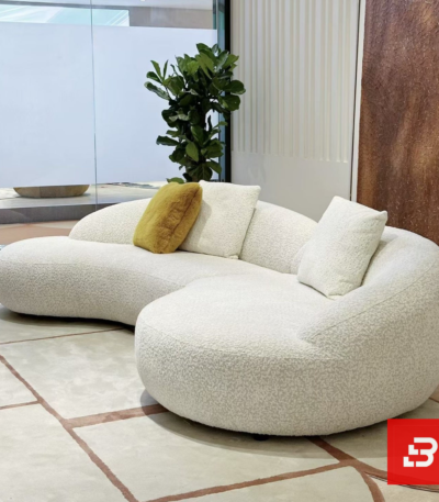 Modern interior view of a luxury organic curved sofa upholstered in textured off white bouclé fabric featuring fluid rounded contours and accent pillows by Bahoo Furniture UAE