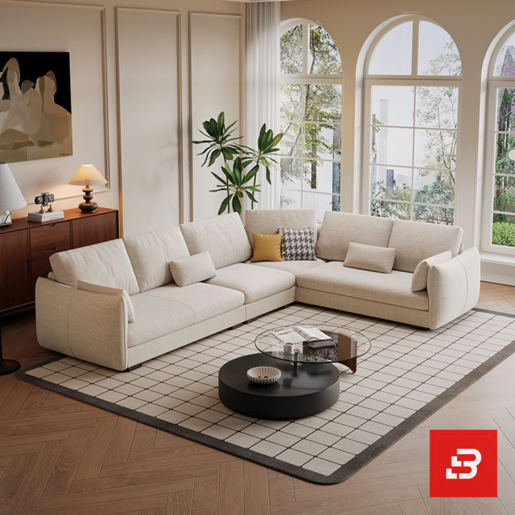Spacious bright living room interior view of a luxury l-shaped sectional sofa upholstered in textured beige fabric featuring corner configurations and accent cushions by Bahoo Furniture UAE