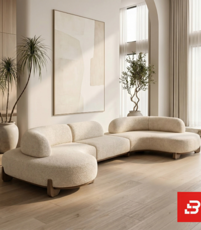 Sunlit luxury living room interior view of a luxury modular curved sofa upholstered in textured off white bouclé fabric featuring fluid wooden base detailing by Bahoo Furniture UAE