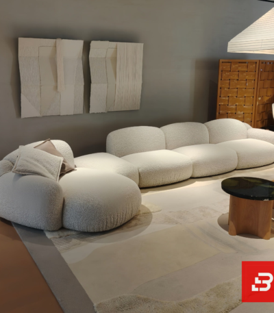 Modern showroom interior view of a luxury upholstered curved modular sofa in textured off white bouclé fabric featuring an organic shape and scatter cushions by Bahoo Furniture UAE