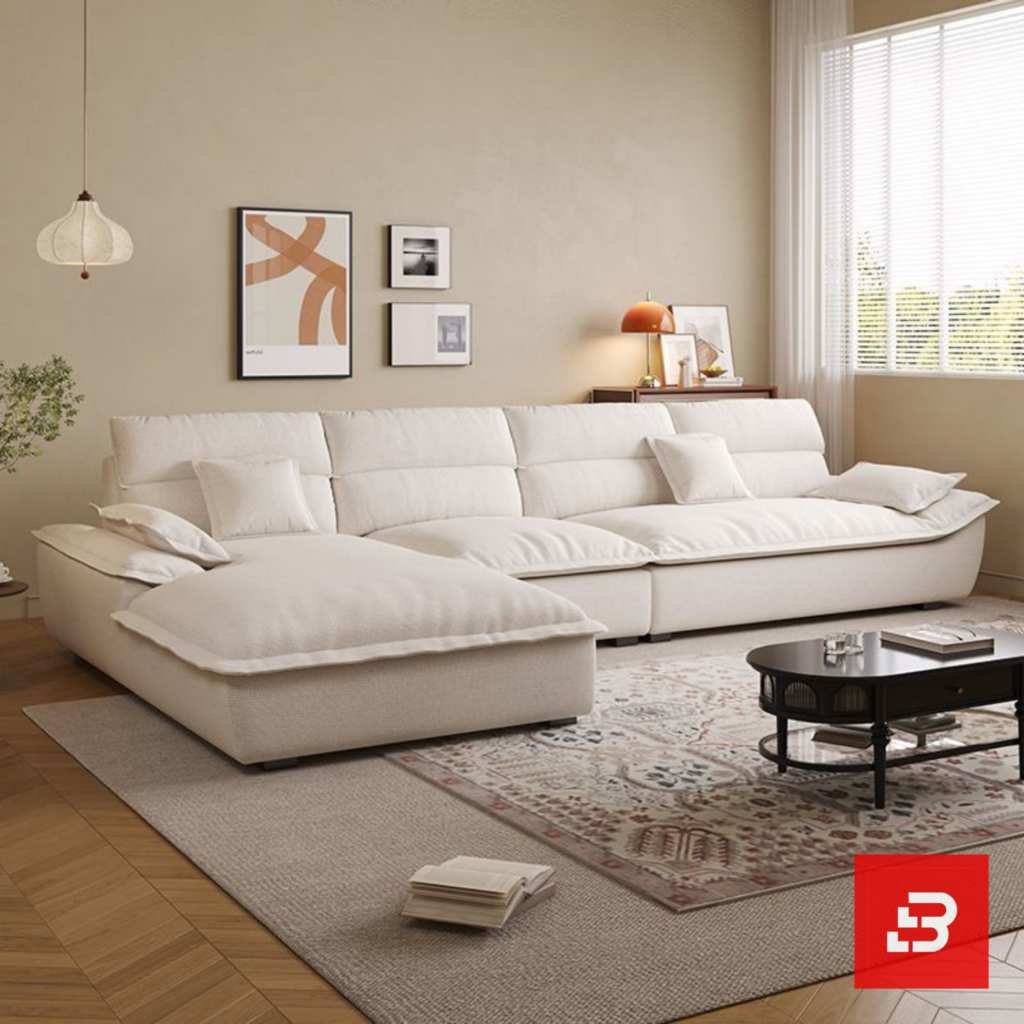 Sunlit luxury living room interior view of a luxury plush cushion sofa upholstered in soft off white fabric featuring deep channeled cushions and matching throw pillows by Bahoo Furniture UAE