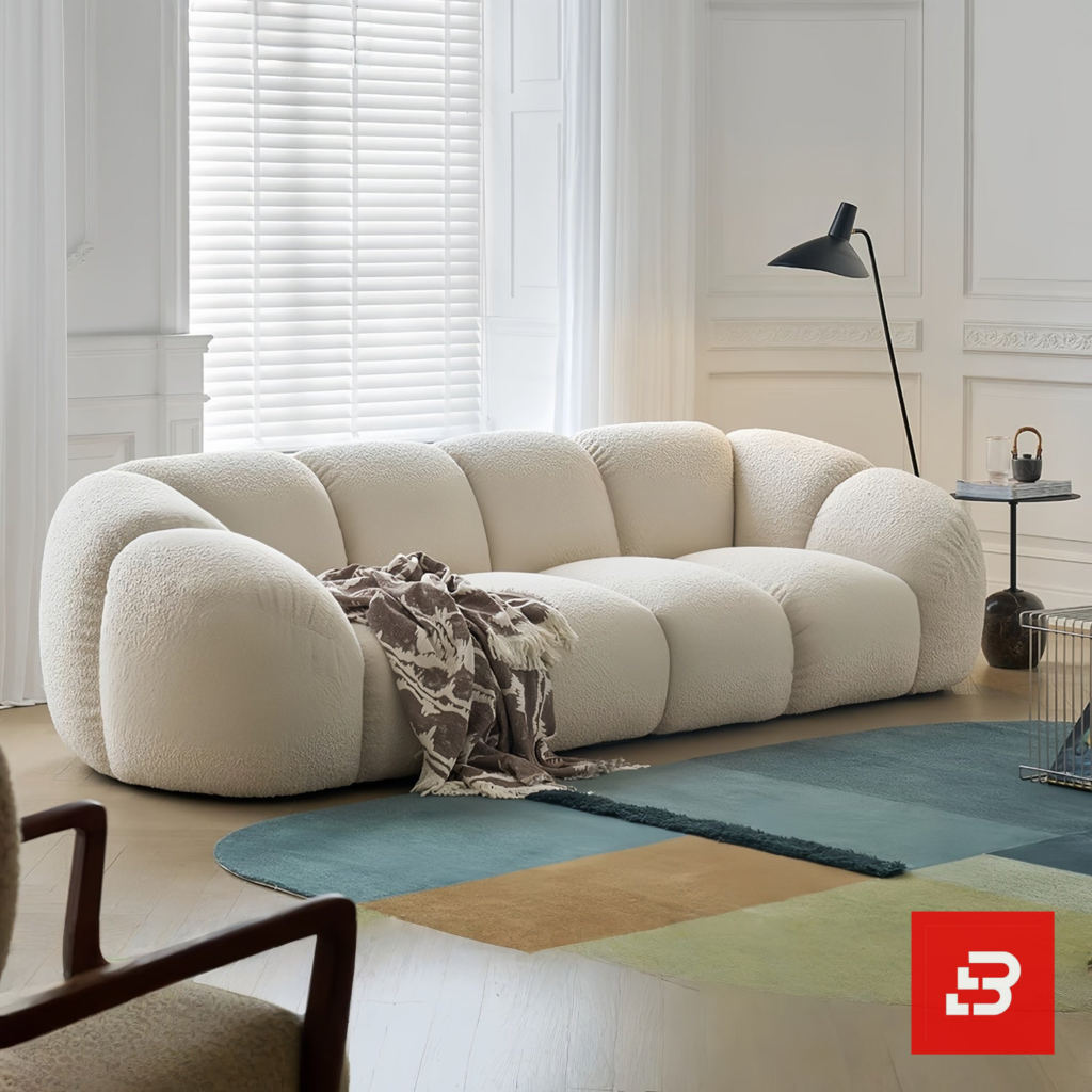 Bright modern minimal living room interior view of a luxury puffy channel sofa upholstered in textured off white bouclé fabric featuring rounded modular compartments and a throw blanket by Bahoo Furniture UAE
