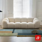 Bright modern minimal living room interior view of a luxury puffy channel sofa upholstered in textured off white bouclé fabric featuring rounded modular compartments and a throw blanket by Bahoo Furniture UAE