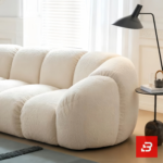 Bright modern minimal living room interior view of a luxury puffy channel sofa upholstered in textured off white bouclé fabric featuring rounded modular compartments and a throw blanket by Bahoo Furniture UAE