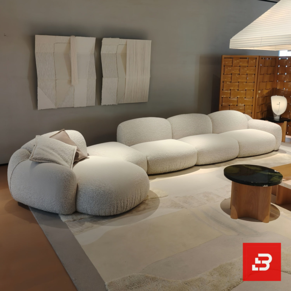 Modern showroom interior view of a luxury upholstered curved modular sofa in textured off white bouclé fabric featuring an organic shape and scatter cushions by Bahoo Furniture UAE