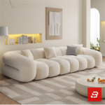 Bright warm living room interior view of a luxury ribbed modular sofa upholstered in textured off white bouclé fabric featuring distinct vertical channeled rolls and accent cushions by Bahoo Furniture UAE