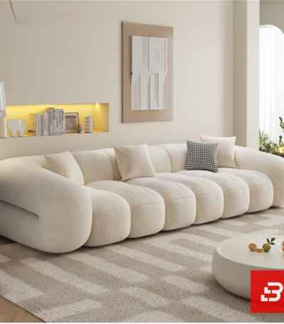 Bright warm living room interior view of a luxury ribbed modular sofa upholstered in textured off white bouclé fabric featuring distinct vertical channeled rolls and accent cushions by Bahoo Furniture UAE