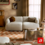Warm modern apartment living room interior view of a luxury l-shaped sectional sofa upholstered in textured off white bouclé fabric featuring an extended chaise lounge and rust accent pillows by Bahoo Furniture UAE