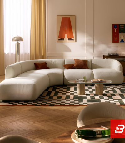 Sunlit modern luxury villa living room interior view of a luxury u-shaped modular sectional upholstered in textured off white bouclé fabric featuring a matching ottoman and rust throw pillows by Bahoo Furniture UAE