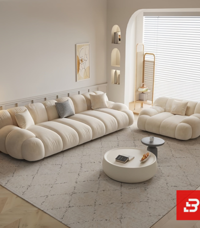 Bright modern sunlit living room interior view of a luxury channel modular lounge set upholstered in textured off white bouclé fabric featuring horizontal ribbed modules, an armchair, and an ottoman by Bahoo Furniture UAE