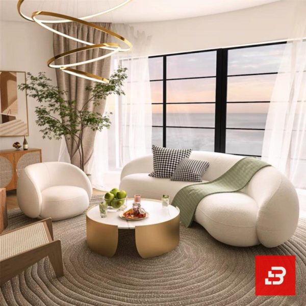Stunning seaside modern luxury living room interior view of a luxury curved asymmetric sofa upholstered in textured off white bouclé fabric featuring a matching armchair and golden round coffee table by Bahoo Furniture UAE