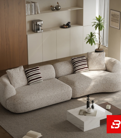 Elegant modern minimalist living room interior showcasing an asymmetric curved sofa upholstered in textured beige bouclé fabric featuring speckled details and stylish striped accent pillows by Bahoo Furniture UAE