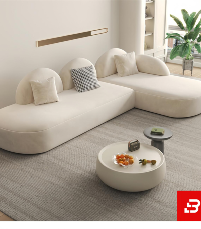 Bright modern minimalist living room interior showcasing an L-shaped modular sectional sofa upholstered in textured off white bouclé fabric featuring distinct half-moon backrests and accent pillows by Bahoo Furniture UAE