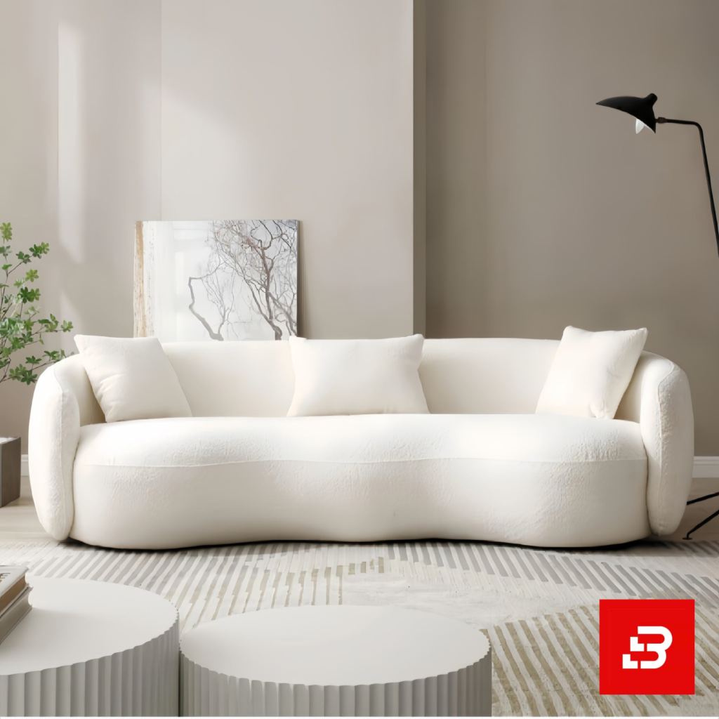 Sunlit modern minimalist living room interior showcasing a luxury curved sofa upholstered in textured off white bouclé fabric featuring sweeping rounded armrests and matching throw pillows by Bahoo Furniture UAE