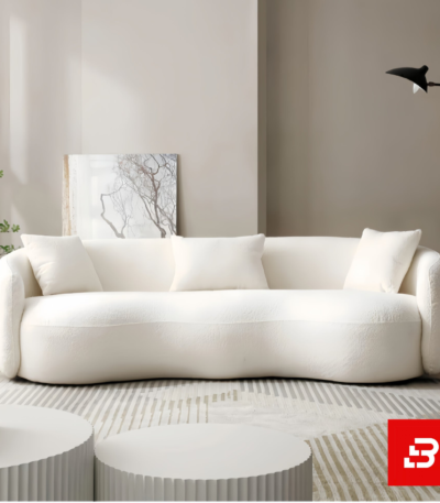 Sunlit modern minimalist living room interior showcasing a luxury curved sofa upholstered in textured off white bouclé fabric featuring sweeping rounded armrests and matching throw pillows by Bahoo Furniture UAE