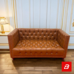Classic elegant living room interior showcasing a luxury chesterfield sofa upholstered in rich beige leather fabric featuring deep button tufting and rolled arms by Bahoo Furniture UAE