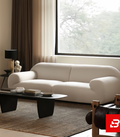 Bright modern minimalist living room interior showcasing a luxury curved sofa upholstered in textured off white bouclé fabric featuring sweeping rounded armrests and sleek dark wood coffee table by Bahoo Furniture UAE