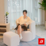 Bright modern living room interior showcasing a luxury accent armchair and matching ottoman upholstered in soft off white bouclé fabric featuring a decorative checkered throw pillow by Bahoo Furniture UAE